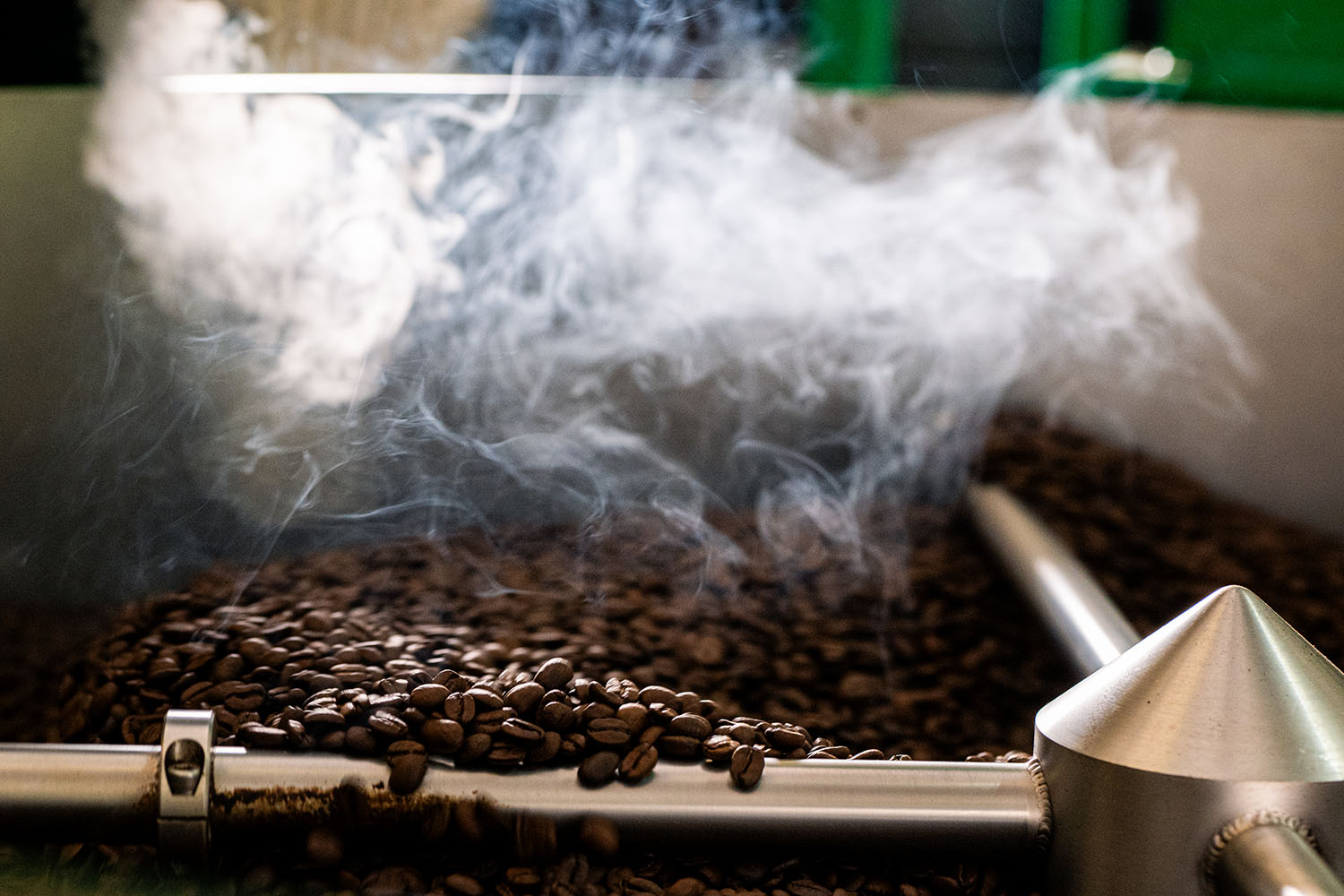 Coffee beans being roasted with smoke rising from a roasting machine.